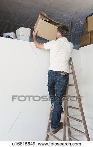 Stock Photo - tarifa, cadiz, andalusia, spain; a man on a step ladder tidying up the attic. Fotosearch
