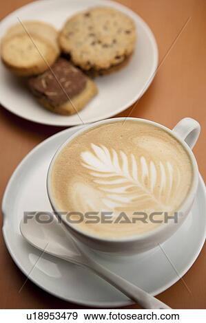 Stock Photo - Afternoon tea, Coffee, Close-up of a cup of cappuccino with pattern and dessert on the saucer. Fotosearch