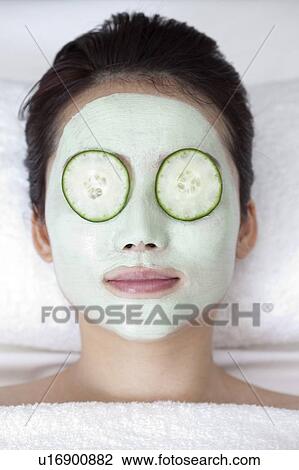 Stock Image - Beauty Treatment, Close-up of woman's face with lotion and cucumber for skin care. Fotosearch