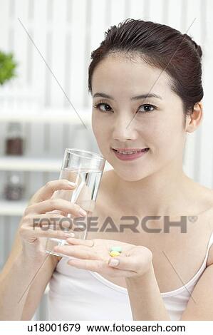 Stock Photo - Beauty Treatment, Woman holding a glass of water and pills with smile. Fotosearch