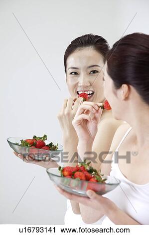 Stock Image - Beauty Treatment, Woman looking at the mirror and eating a plate of strawberry. Fotosearch