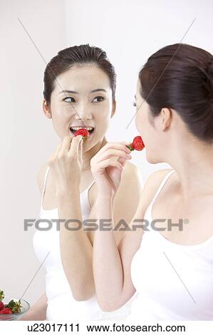 Stock Image - Beauty Treatment, Woman looking at the mirror and eating a strawberry. Fotosearch