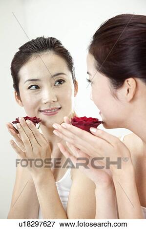 Stock Photo - Beauty Treatment, Woman looking at the mirror and holding a red rose with smile. Fotosearch