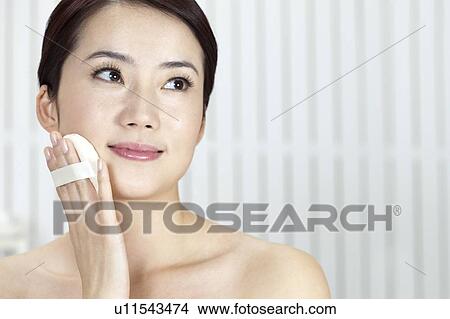Picture - Beauty Treatment, Woman looking away and holding powder puff on face. Fotosearch