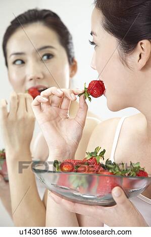 Stock Photograph - Beauty Treatment, Woman looking into mirror and eating a plate of strawberry. Fotosearch