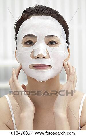 Stock Photo - Beauty Treatment, Woman putting facial mask on her face and looking at the camera. Fotosearch
