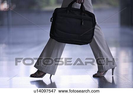 Close-up of businesswoman walking and holding a briefcase View Large Photo Image Stock Photo - Close-up of businesswoman walking and holding a briefcase. Fotosearch