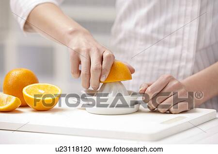 Stock Image - Close-up of hands pressing an orange on juicer. Fotosearch