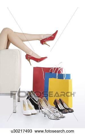 Stock Image - Close-up of young woman's legs, several high heels and shopping bags. Fotosearch