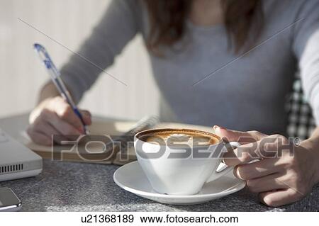 Coffee Break, Young woman holding a cup of coffee and writing on a notebook View Large Photo Image Stock Photo - Coffee Break, Young woman holding a cup of coffee and writing on a notebook. Fotosearch