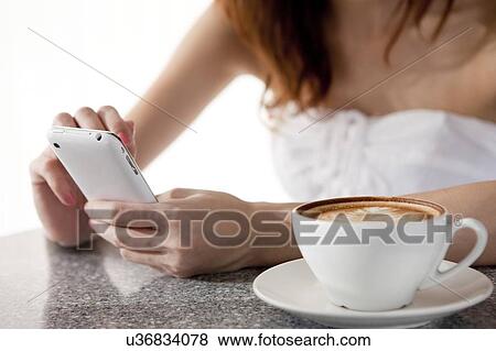 Stock Photo - Coffee Break, Young woman using mobile phone with a cup of coffee beside. Fotosearch