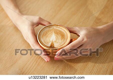 Stock Image - Coffee Culture, Close-up of hands holding a cup of coffee with heart shape. Fotosearch