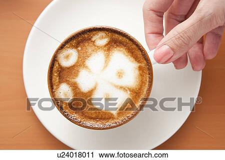 Stock Image - Coffee, Human hand holding a cup of cappuccino with pattern. Fotosearch