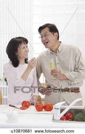 Stock Image - Couple, Couple eating food in kitchen and smiling happily. Fotosearch