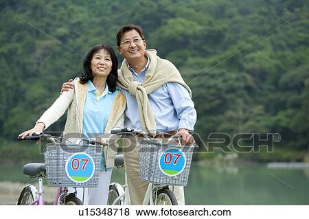Stock Photo - Couple, Couple holding bikes and looking up with smile. Fotosearch