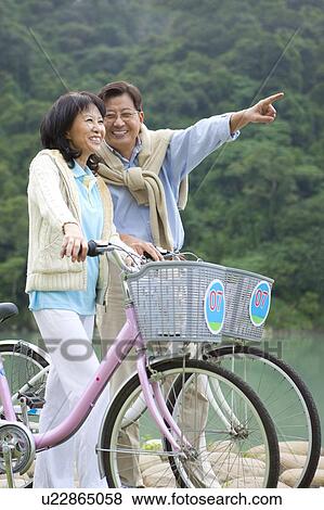 Couple, Couple holding bikes and looking away with smile View Large Photo Image Stock Photo - Couple, Couple holding bikes and looking away with smile. Fotosearch