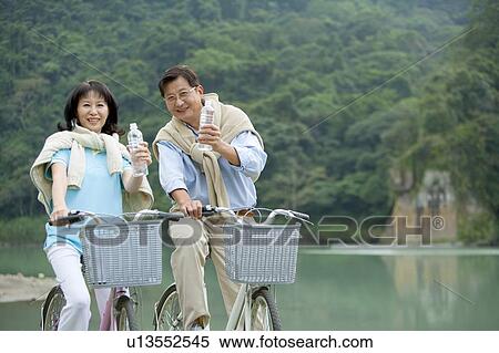 Stock Photography - Couple, Couple riding on bike and holding a bottle water. Fotosearch