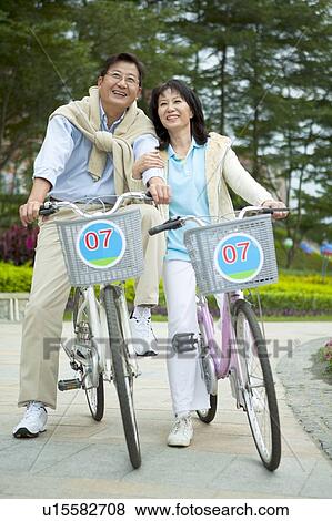Stock Photo - Couple, Couple riding on bikes and looking up with smile. Fotosearch