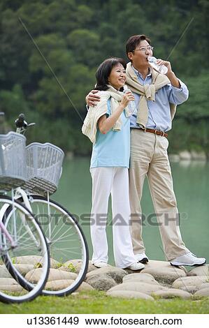 Stock Photo - Couple, Couple standing near the lake and drinking water. Fotosearch