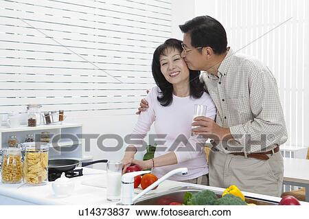 Stock Photo - Couple, Husband kissing wife in the kitchen and holding a glass of milk. Fotosearch