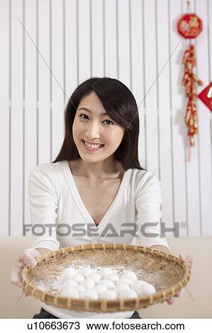 Stock Image - New Year, Young woman holding a bamboo sieve with stuffed dumplings and smiling at the camera. Fotosearch