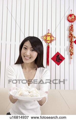Stock Photo - New Year, Young woman holding a plate of dumplings and smiling at the camera. Fotosearch