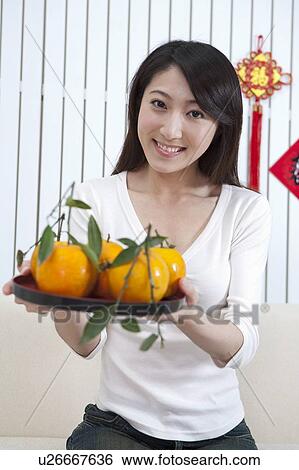 Stock Photograph - New Year, Young woman holding a plate of oranges and smiling at the camera. Fotosearch