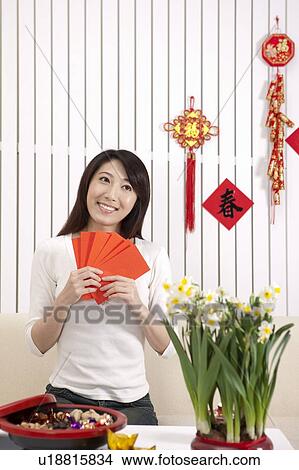 Picture - New Year, Young woman holding red envelopes and looking away with smile. Fotosearch