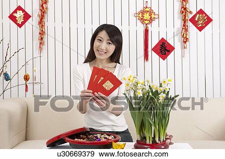 Stock Photo - New Year, Young woman holding red envelopes and smiling at the camera. Fotosearch