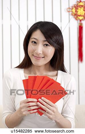 Stock Photography - New Year, Young woman holding red envelopes and smiling at the camera. Fotosearch