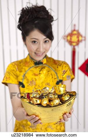 New Year, Young woman wearing Chinese traditional clothing and holding gold ingots with smile View Large Photo Image Picture - New Year, Young woman wearing Chinese traditional clothing and holding gold ingots with smile. Fotosearch