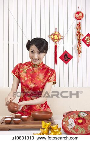 Stock Image - New Year, Young woman wearing Chinese traditional clothing and making tea culture with smile. Fotosearch