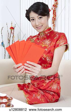 Stock Image - New Year, Young woman wearing Chinese traditional clothing and holding red envelopes with smile. Fotosearch