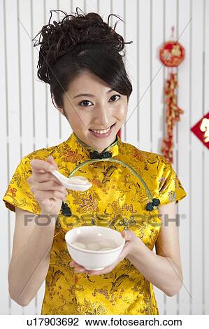 Stock Image - New Year, Young woman wearing Chinese traditional clothing and holding a bowl of stuffed dumplings with smile. Fotosearch
