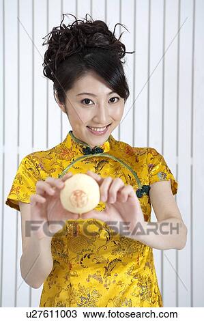 Stock Image - New Year, Young woman wearing Chinese traditional clothing and holding the snack with smile. Fotosearch