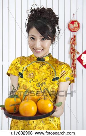 Stock Photo - New Year, Young woman wearing Chinese traditional clothing and holding a plate of oranges with smile. Fotosearch