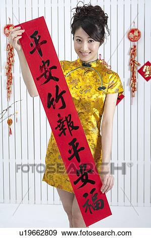 Stock Photo - New Year, Young woman wearing Chinese traditional clothing and holding couplet with smile. Fotosearch