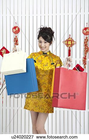 Stock Photo - New Year, Young woman wearing Chinese traditional clothing and holding shopping bags with smile. Fotosearch
