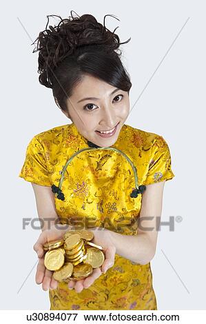 Stock Photo - New Year, Young woman wearing Chinese traditional clothing and holding a stack of gold coins with smile. Fotosearch