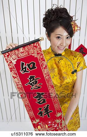 Stock Photograph - New Year, Young woman wearing Chinese traditional clothing and holding the couplet with smile. Fotosearch
