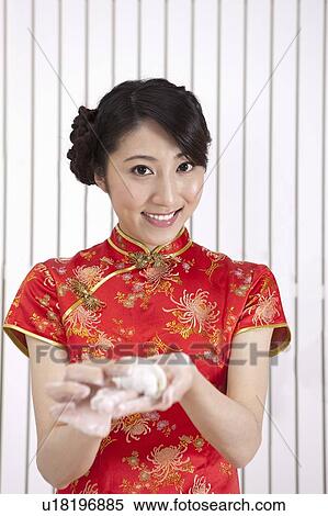 Stock Photography - New Year, Young woman wearing Chinese traditional clothing and holding dumpling with smile. Fotosearch