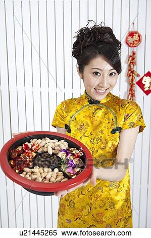 Stock Photography - New Year, Young woman wearing Chinese traditional clothing and holding a plate of snacks with smile,. Fotosearch