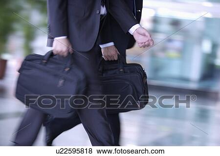 Stock Photo - Two businessmen walking and holding briefcase together. Fotosearch