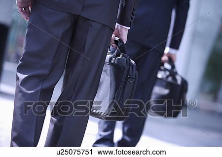 Two businessmen well-dressed standing and holding briefcase View Large Photo Image Stock Image - Two businessmen well-dressed standing and holding briefcase. Fotosearch