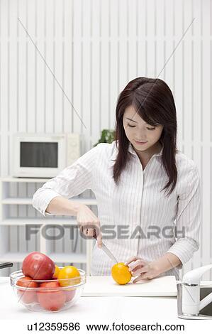 Stock Photograph - Woman cutting an orange in the kitchen. Fotosearch