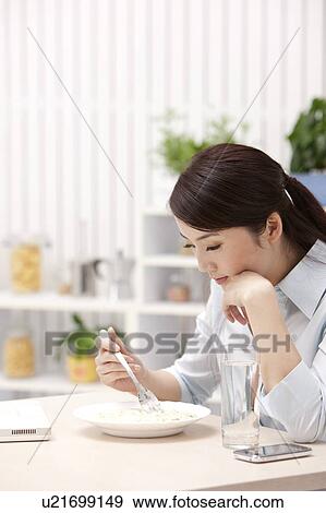 Woman eating food with fork and looking down with hand on chin View Large Photo Image Stock Photo - Woman eating food with fork and looking down with hand on chin. Fotosearch