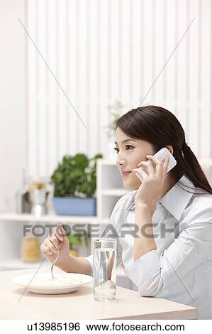 Stock Photograph - Woman eating on the table and using mobile phone. Fotosearch