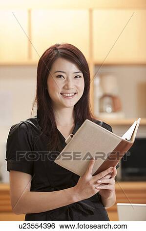 Stock Photograph - Woman holding a book and looking at the camera with smile. Fotosearch
