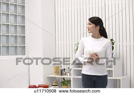 Stock Photo - Woman holding a cup and looking away with smile. Fotosearch
