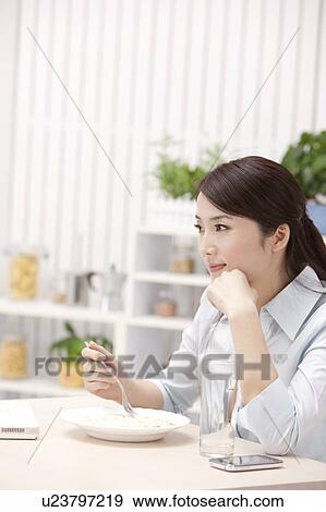 Stock Photo - Woman holding fork and looking away with hand on chin. Fotosearch